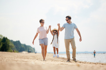 Full length portrait of  happy family playing with cute little girl while enjoying walk on beach during Summer vacation
