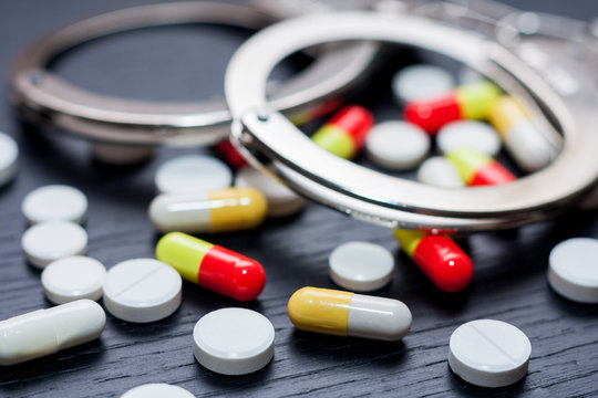 Handcuffs and pills and drugs on wooden table