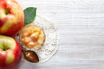 Small dish with apple jam with whole apples and a spoon on a white wooden table, selective focus