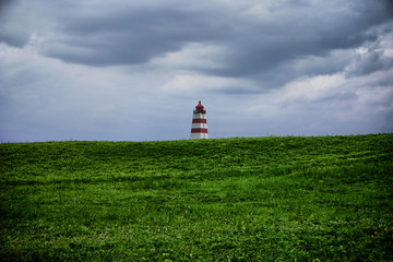 Fototapeta na wymiar Landscape of a stormy day with a lighthouse upon a hill in the background