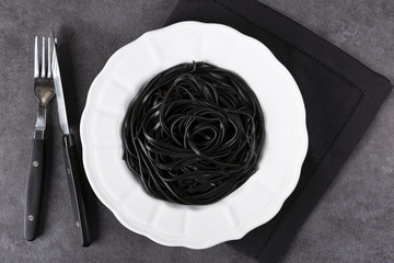 Pasta with wheat germ and black squid ink. Black pasta and parsley on a white plate.  Macro. Top view.