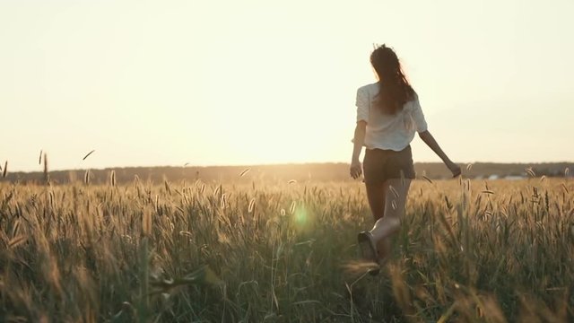 Free young woman running fast in open field, warm summer weather. Shot from behind of running towards sunset girl, majestic nature.