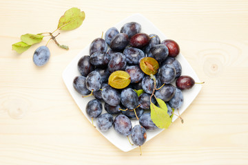 Fresh plums with leaves on a wooden table background, Flat lay composition.