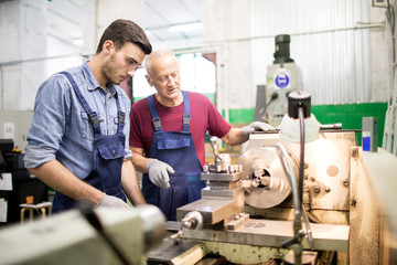 Young engineer looking at rotating detail of industrial machine while his senior colleague...