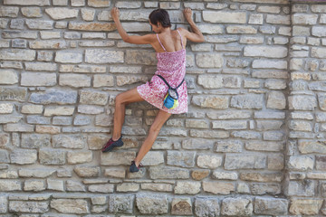 The girl climbs the stone wall.