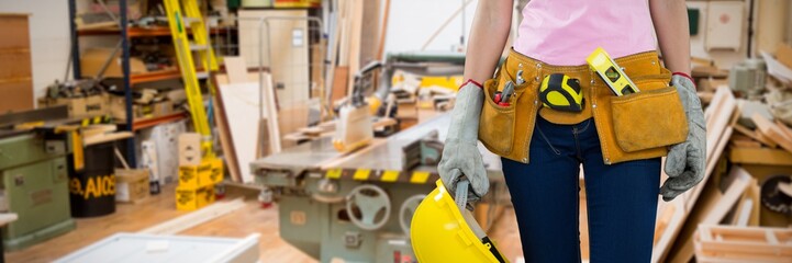 Composite image of woman with tool belt and holding hard hat