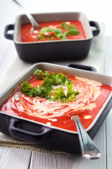 Creamy tomato soup in bowls with spoons on white wooden surface , vertical