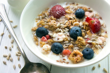 Muesli and yogurt breakfast with fresh strawberries , blueberries and seeds closeup on white wooden table