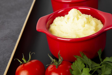 Food is still life. Two red pots with potato puree and fried vegetables on a black tray. Background black marble.