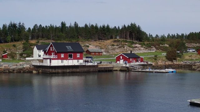 Red wooden house on the shore of the Norwegian fjord in sunny weather, Averoy, Norway
