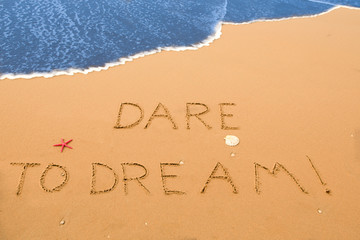 Fototapeta premium dare to dream written in the sand on a sunny beach