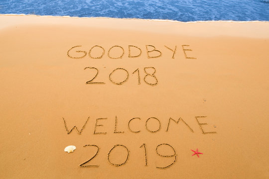 goodbye 2018 and welcome 2019 written in the sand on a sunny beach near the surf