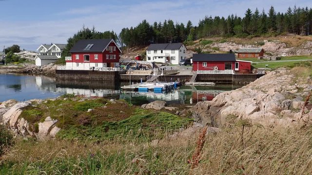 Red wooden house on the shore of the Norwegian fjord in sunny weather, Averoy, Norway
