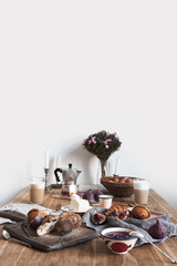 Breakfast in modern kitchen with croissants, figs, coffee, bread on board over rustic wooden table background, empty space on white wall