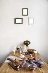 Breakfast in kitchen with photo frames on white wall. Croissants, figs, coffee, bread on wooden table background, empty space for layout