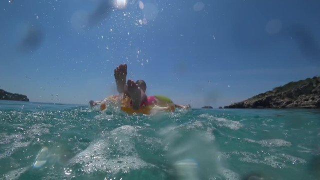 Attractive girl having fun on inflatable ring and splashing water. Underwater 4K shot