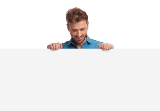 smiling casual man holding blank board looks down at it