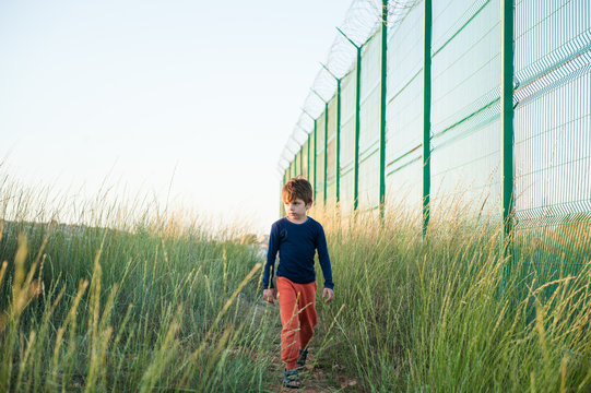 one little boy refugee walking along high fence with razor wire news report