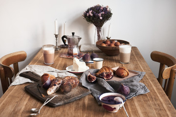 Breakfast in modern kitchen with croissants, figs, coffee, bread on board over rustic wooden table background, ceramics dishes, warm colors