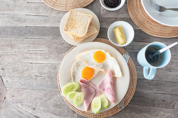 Breakfast egg and ham on white plate and coffee on wooden table .