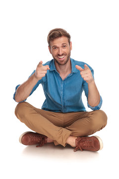 happy man sitting on the floor is pointing his fingers