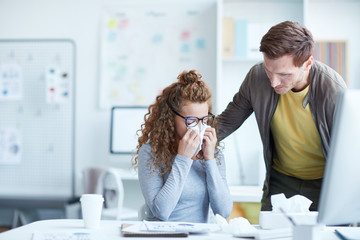 Young businessman leaning over his upset female colleague crying and wiping her tears with paper...