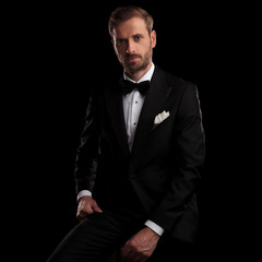 young elegant man in tuxedo resting on a chair