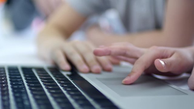 Close up hands of unrecognizable child of primary school age using touchpad of laptop computer when studying in information technology class