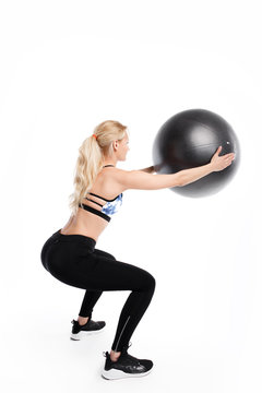 Fit young pretty woman doing squats exercises with fitness ball. Back view.