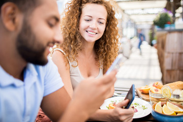 Portrait of modern woman smiling happily while chatting with friend sitting at cafe table outdoors, copy space