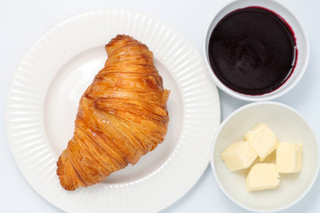 Freshly baked croissant, jam and butter slices on a light background