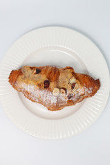 Freshly baked croissant with nuts on a white plate