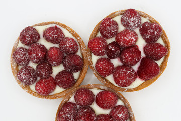 Three tartlets with raspberry on white background