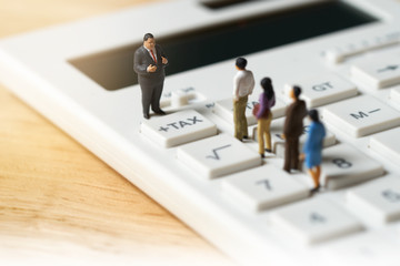 Miniature people Pay queue Annual income (TAX) for the year on calculator. using as background...