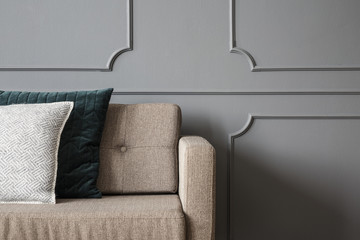 Close-up of pillows on beige sofa against grey wall with molding in living room interior. Real photo