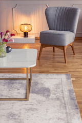 Flowers on table on carpet in apartment interior with grey armchair next to lamp. Real photo