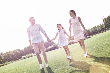 Family walk. Family of three walking on grassy field smiling che