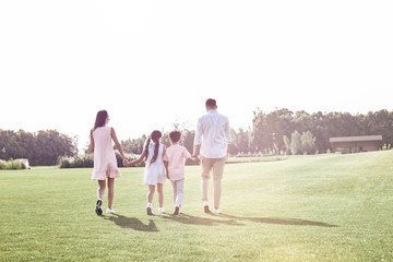 Obraz premium Bonding. Family of four walking on grassy field back view