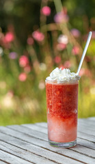 Mixed strawberry with ice and double cream on top in tall glass.