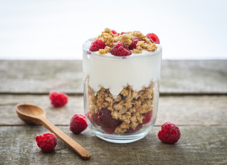 Yogurt with muesli in glass bowl with pieces raspberries on top.