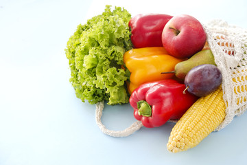 Bunch of mixed organic fruit, vegetables & greens: corn cob, tomato, pepper, lettuce salad leaf, pear, plum and apples in reusable cotton net bag. Zero waste concept. Background, copy space, close up.