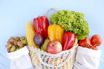 Bunch of mixed organic fruit, vegetables & greens: corn cob, tomato, pepper, lettuce salad leaf, pear, plum and apples in reusable cotton net bag. Zero waste concept. Background, copy space, close up.