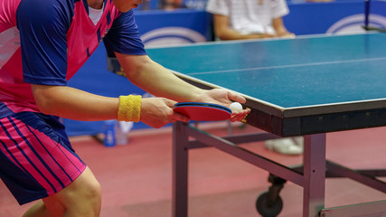 a pink shirt man is serving a ball during a table tennis game