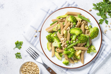 Vegan pasta penne with broccoli, avocado and pine nuts top view.