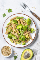 Vegan pasta penne with broccoli, avocado and pine nuts top view.