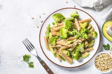 Vegan pasta penne with broccoli, avocado and pine nuts top view.