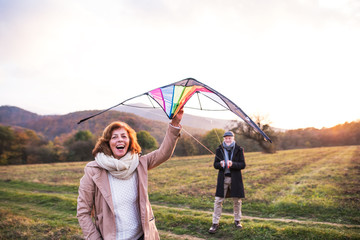 Carefree senior couple flying a kite in an autumn nature at sunset.