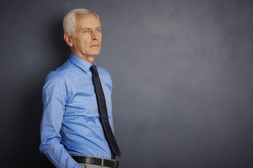 Fototapeta premium Senior man portrait. Shot of an elderly businessman wearing suit and looking up while standing at grey background. 