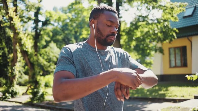 african american man run listen music in headphones using smartwatch smile at park sunshine training active athlete body exercise fit health sport workout runner summer app muscular jogging