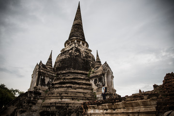 Obraz premium A western traveler boy observes the ruins of the temples in the old capital of Ayutthaya in the background of a storm coming